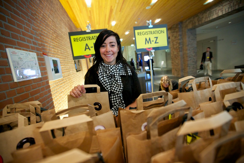 A woman stands behinds bags at a registration table.